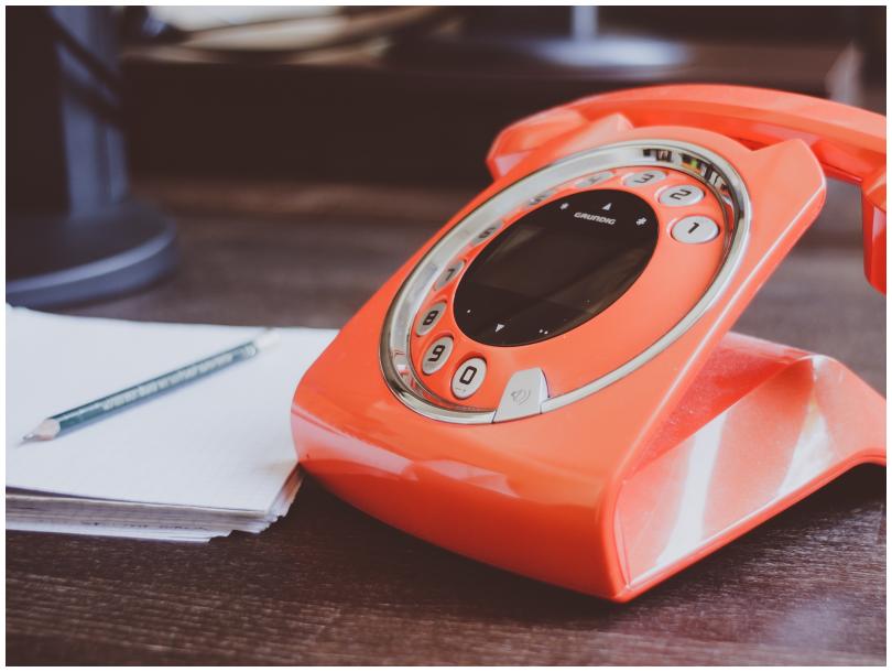 Orange vintage landline phone and a notebook with a pencil on it on a wooden table