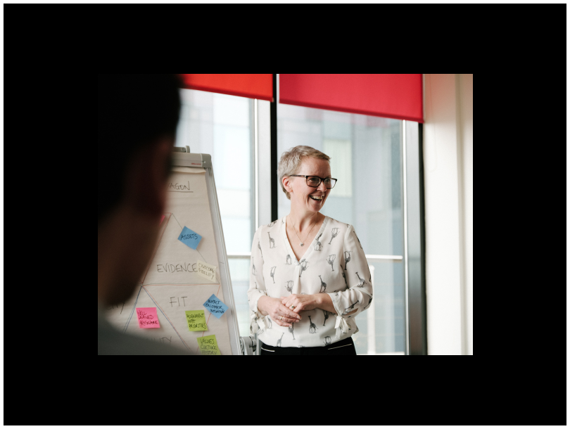 White woman in white blouse standing by a flip chart with a smile on her face