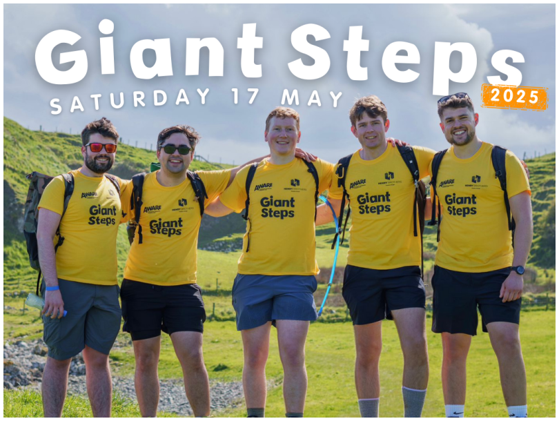 A promotional image featuring 4 men wearing AWARE NI t-shirts, walking boots and backpacks with the backdrop of the Causeway Coastline, accompanied by the text 'take Giant Steps along the stunning Causeway Coast for mental health'. The image also includes details about the sponsored 7, 13 or 20-mile coastal hike happening on Saturday 17 May, and the website aware-ni.org/giant to sign up today!