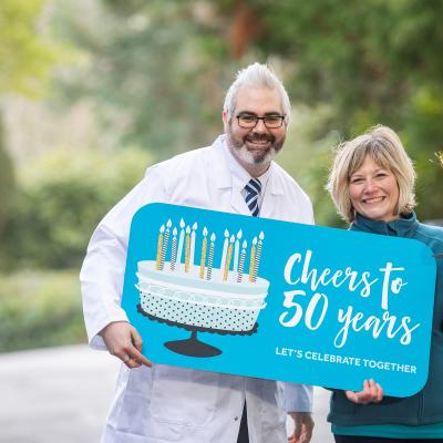 Dr Kienan Savage, senior molecular biologist at QUB, and cancer survivor Emily Stanton encourage everyone to sign up for the Cancer Focus NI Cheers to 50 Years campaign and help raise £100k for locally based cancer research.