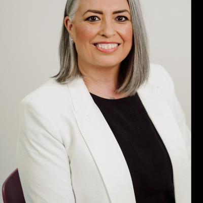 Lady wearing white jacket with black top, grey hair styled in a bob. 